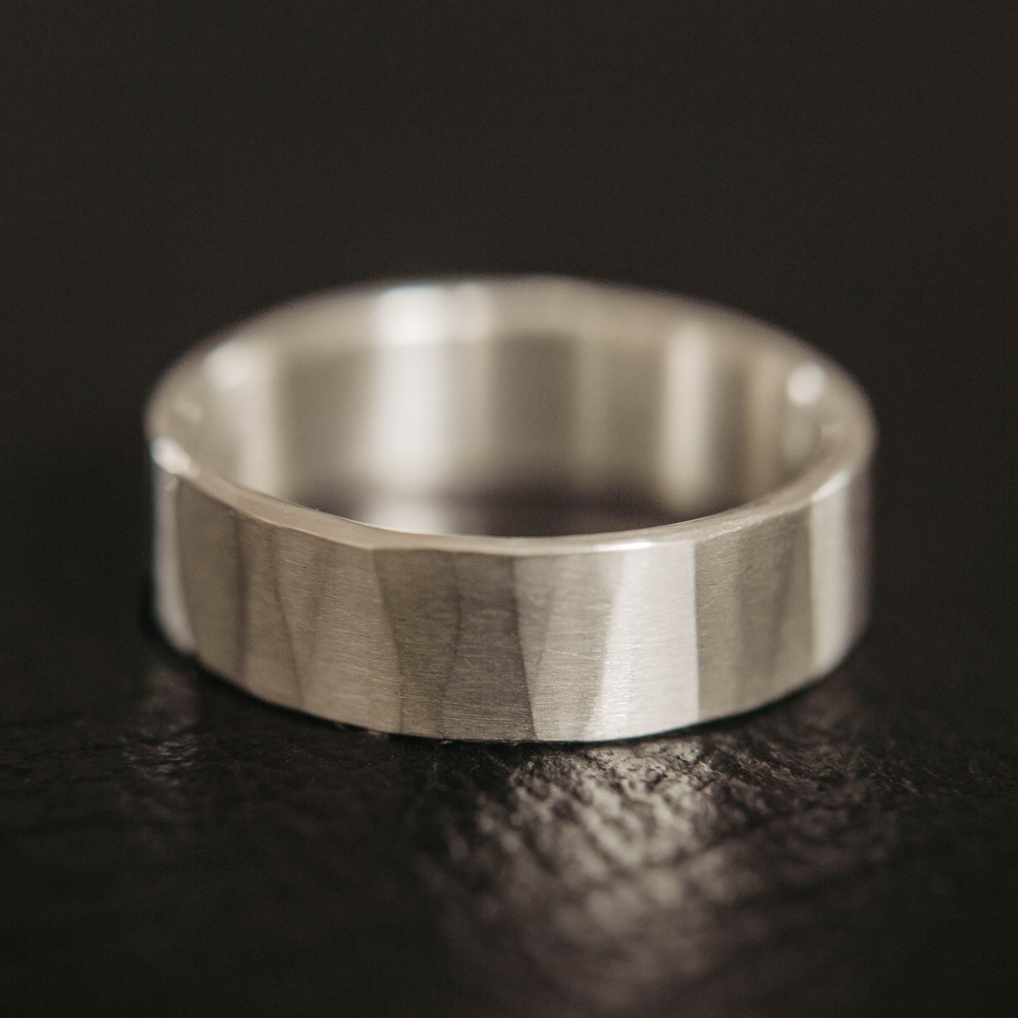 Mens sterling silver wedding band. This photo shows a lightly faceted silver ring (Horizontal with black backdrop)