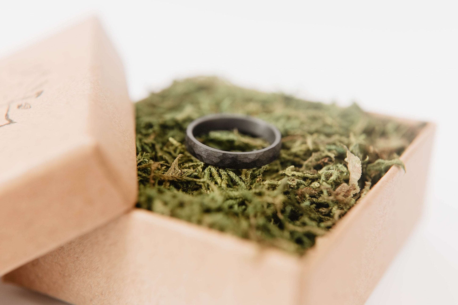 Womens black wedding band. This photo shows a lightly faceted black zirconium ring. (horizontal in ring box with moss))