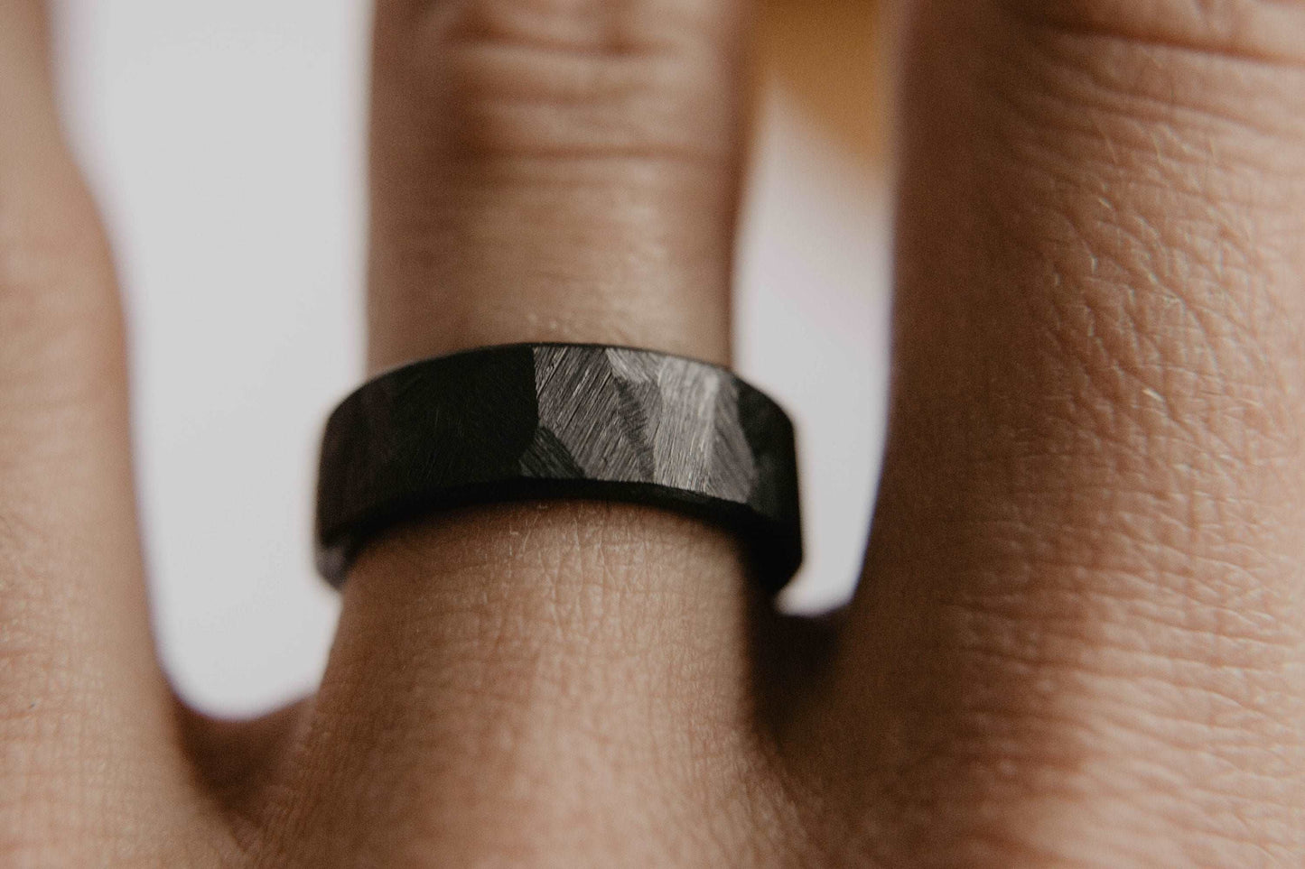 Mens black wedding band. This photo shows a roughly faceted black zirconium ring. (Shown on finger)