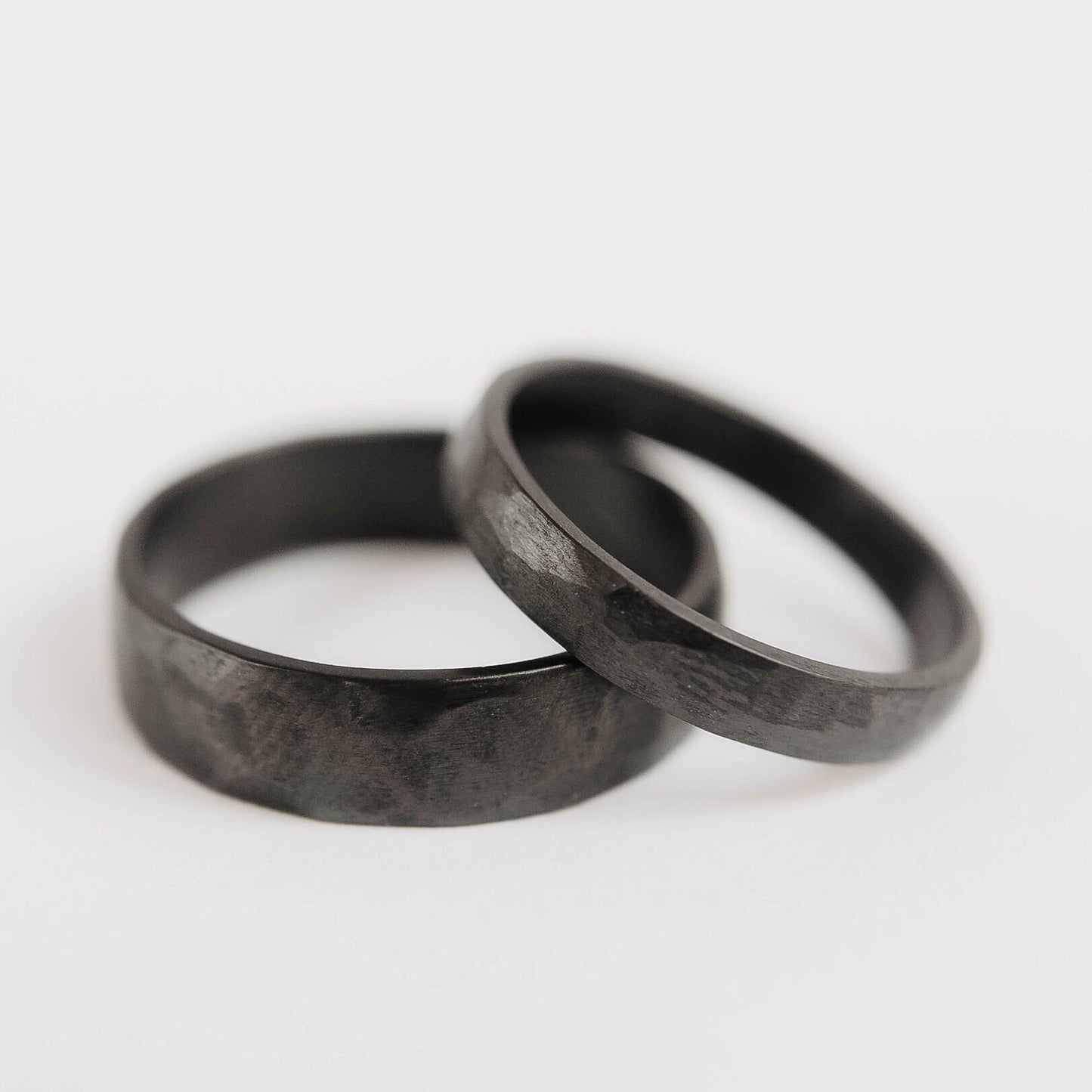 Womens black wedding band. This photo shows a lightly faceted black zirconium ring. (horizontal on top of black mens band)