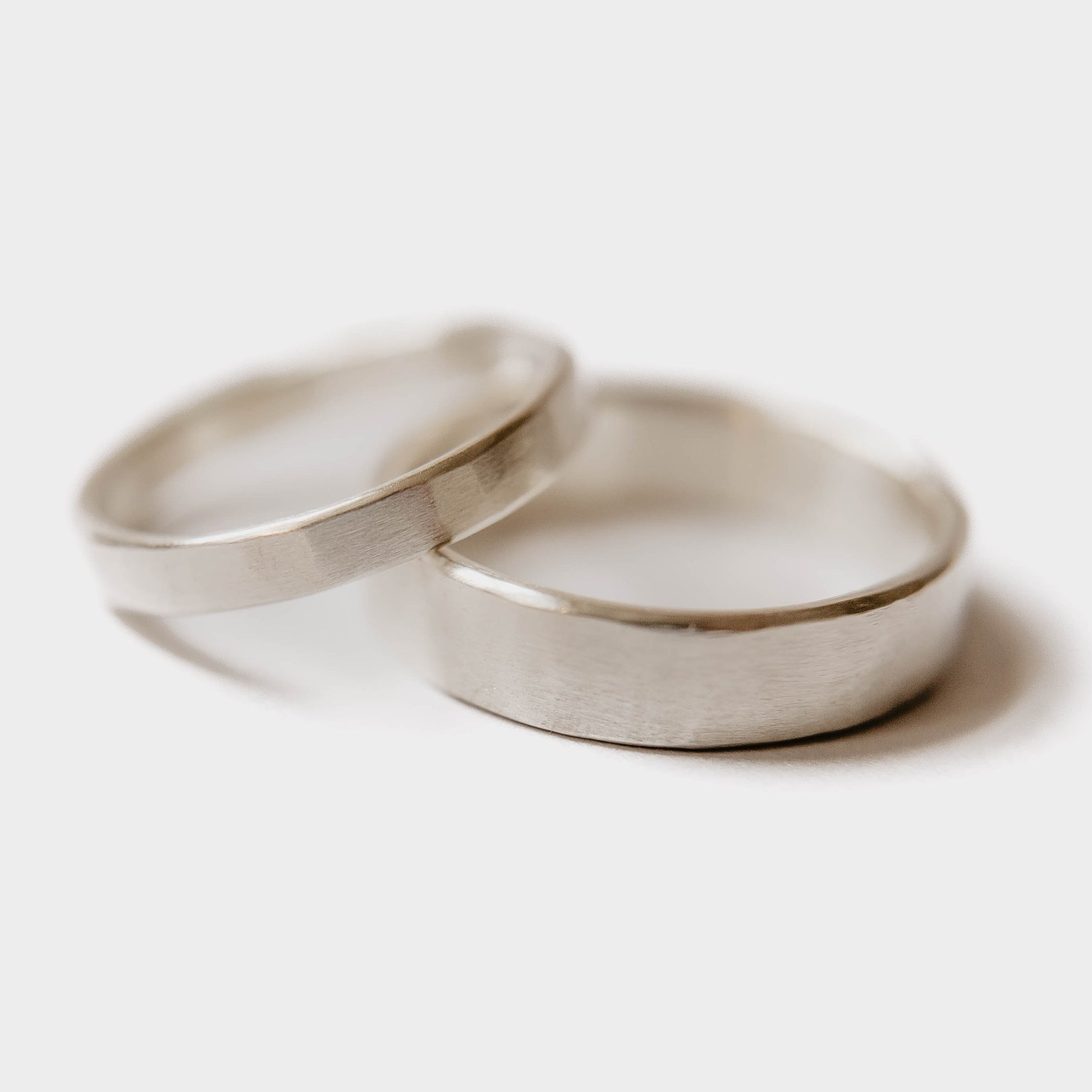 Handmade Silver Wedding Band Set. This photo shows two forged sterling silver rings. (Mens band horizontal Womens band horizontal with white background)
