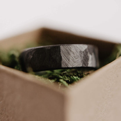 Mens black wedding band. This photo shows a roughly faceted black zirconium ring. (Horizontal in ring box with moss)