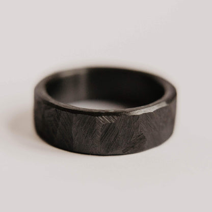 Mens black wedding band. This photo shows a roughly faceted black zirconium ring. (Horizontal with white background)