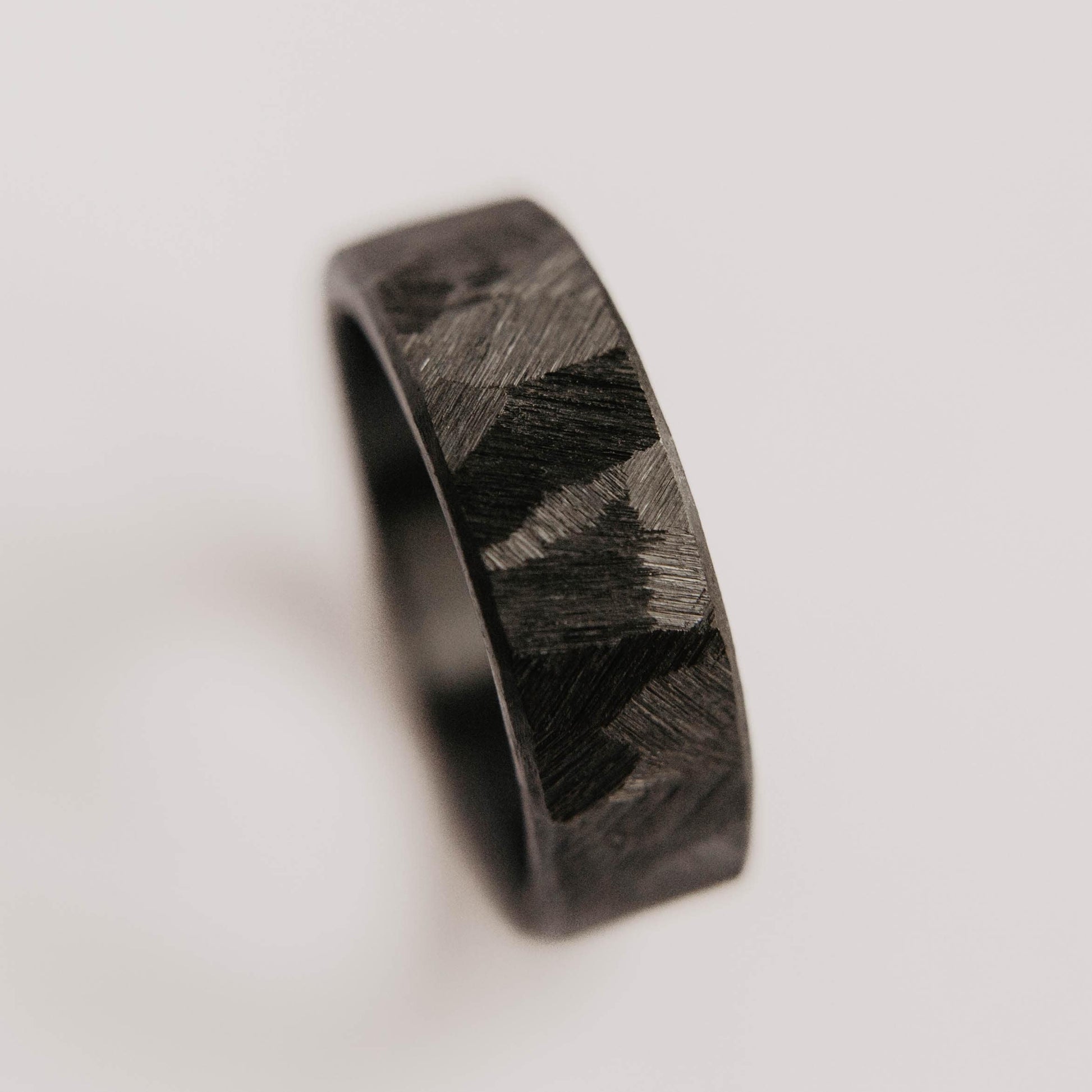 Mens black wedding band. This photo shows a roughly faceted black zirconium ring. (Vertical with white background)