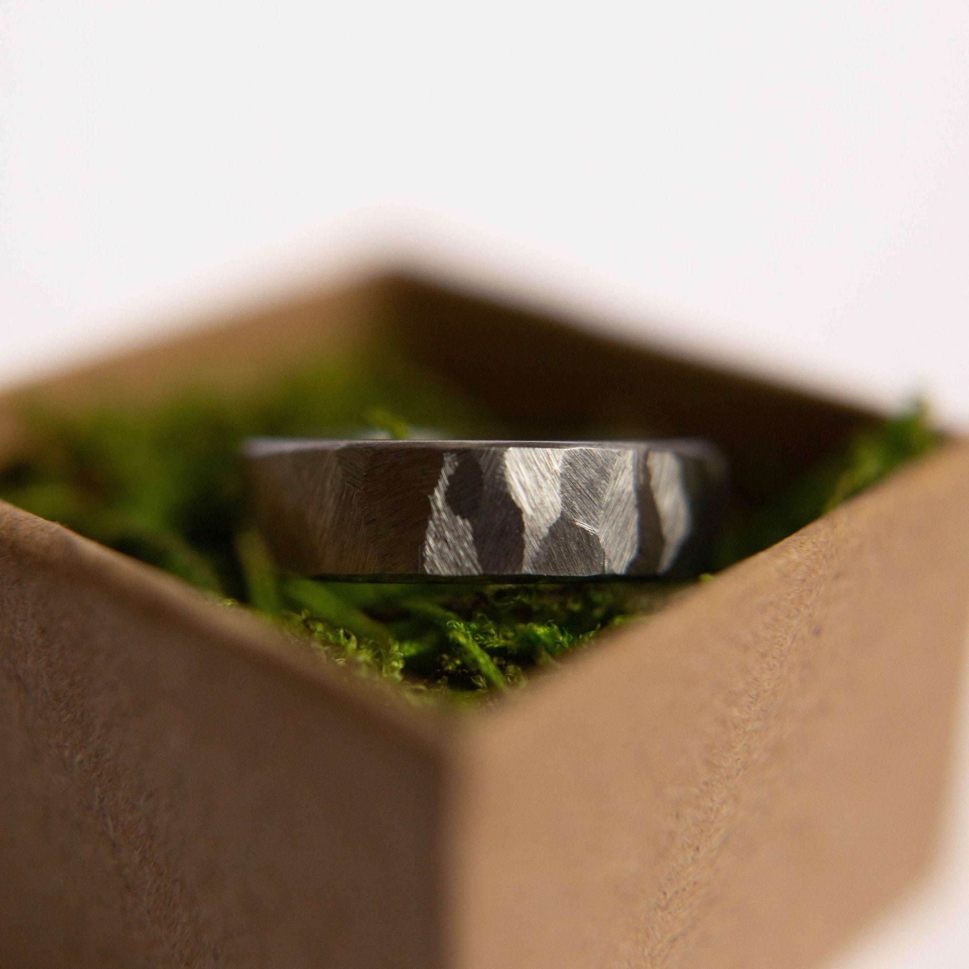 Distressed titanium wedding band. This photo shows a gritty faceted gray titanium ring. (Horizontal in ring box with moss)