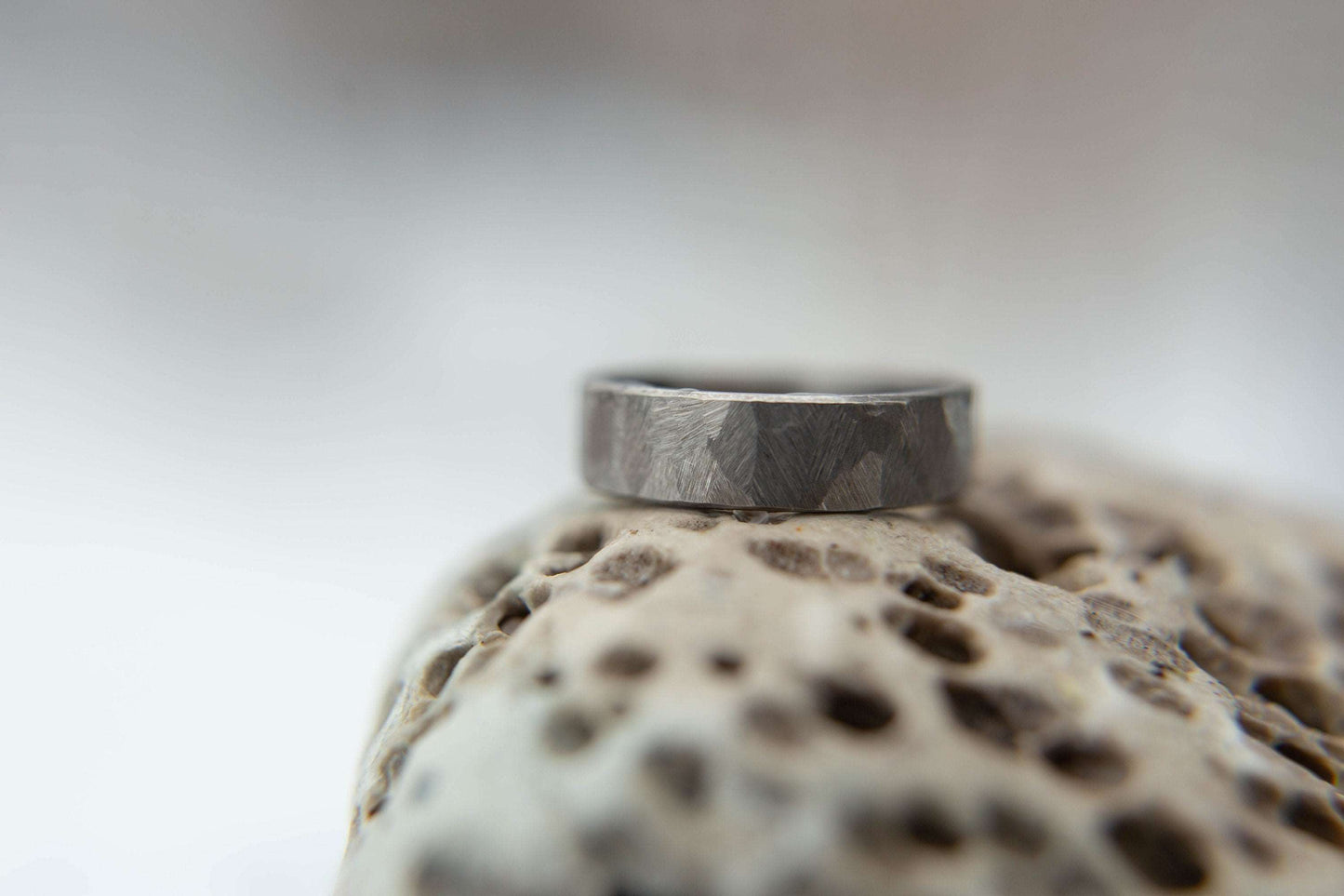 Distressed titanium wedding band. This photo shows a gritty faceted gray titanium ring. (Horizontal on rock)