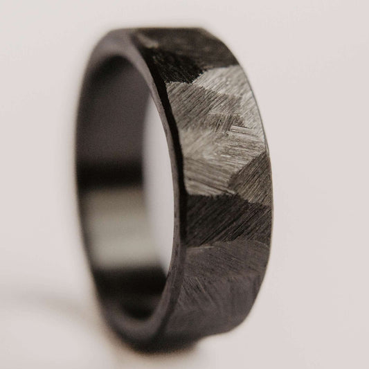 Mens black wedding band. This photo shows a roughly faceted black zirconium ring. (Vertical with white background)