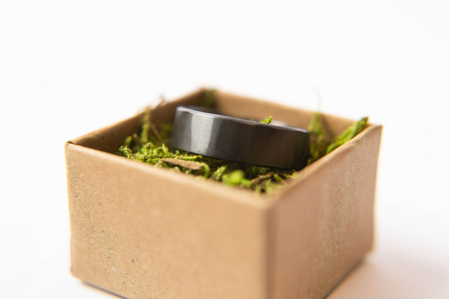 Mens black wedding band. This photo shows a lightly faceted black zirconium ring. (Horizontal in ring box with moss))
