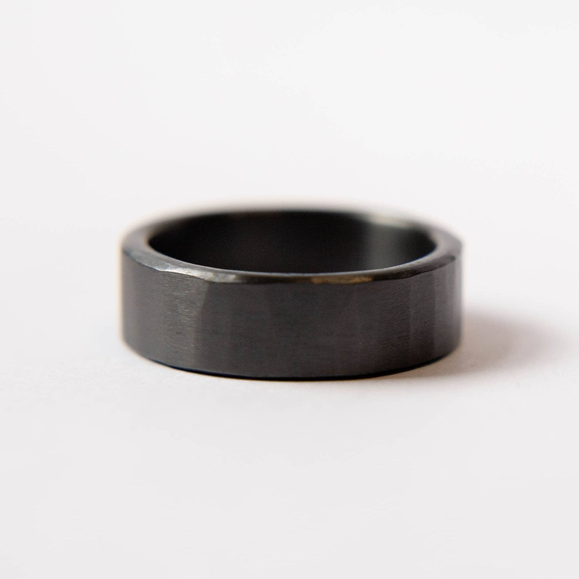 Mens black wedding band. This photo shows a lightly faceted black zirconium ring. (Horizontal with white background)