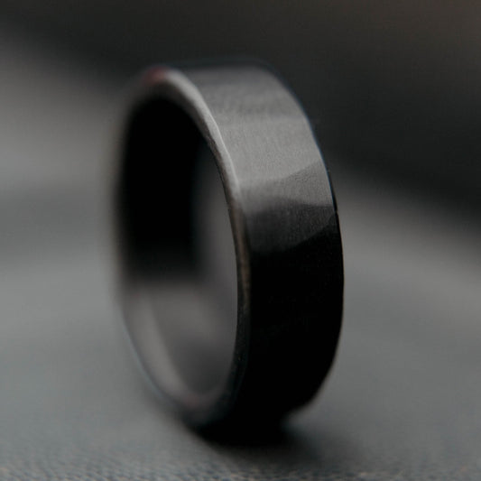 Mens black wedding band. This photo shows a lightly faceted black zirconium ring. (Vertical with black background)